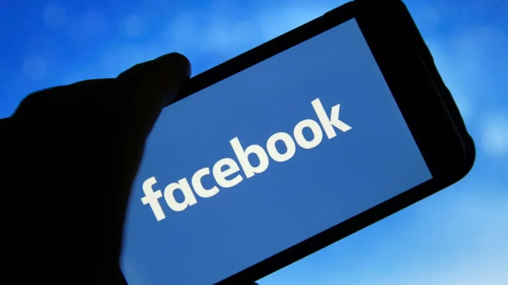 Person holding a mobile phone with Facebook logo on screen.