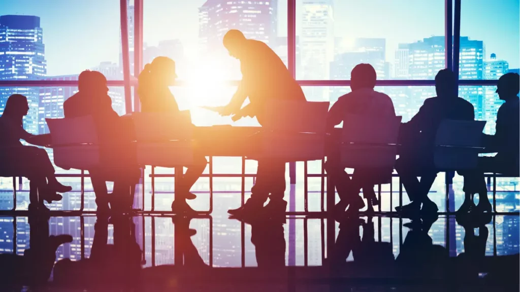 Silhouettes of business professionals in a meeting room with a cityscape background.