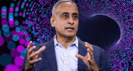 Prabhakar Raghavan speaking at a tech conference with a digital pattern background in blue and purple